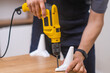 close up hands of skilled furniture assembler attaching legs to a wooden rack in a modern apartment with electric screwdriver 