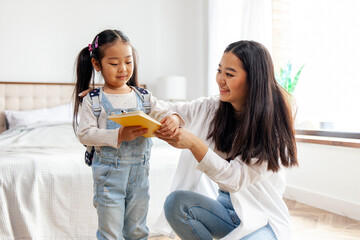 Wall Mural - mother collects Asian daughter to school, woman puts on backpack with book to little girl, back to school