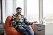 © sofiko14 - Portrait of nice-looking indian employee sitting on soft office chair with personal laptop on knees and smiling at camera. Imposing dark haired man taking short break after intensive working day.