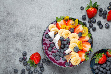 Wall Mural - Healthy summer acai smoothie bowl with chia seeds, fresh banana, strawberry, blueberry, cocos, kiwi top view on rustic concrete background with spoon. Space for text