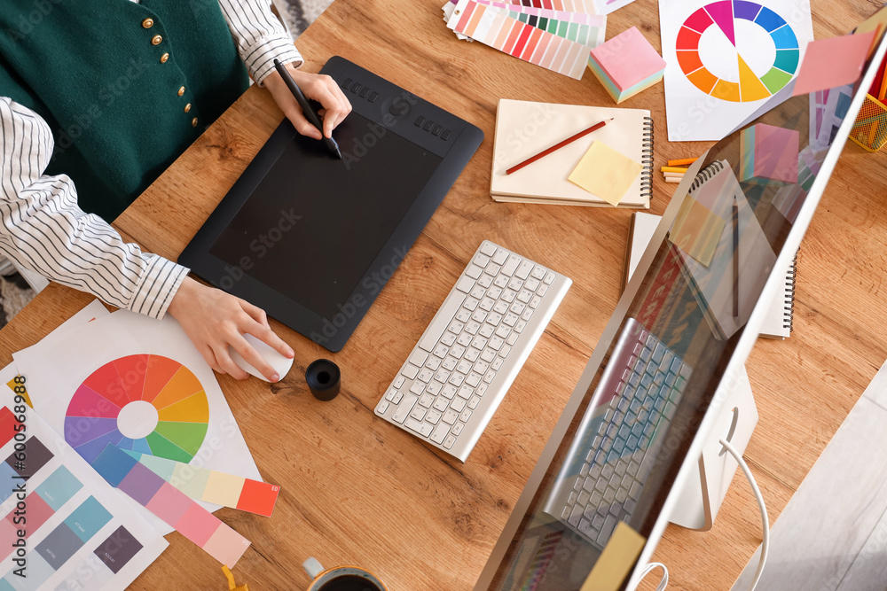 Female graphic designer working with tablet on table in office, top view