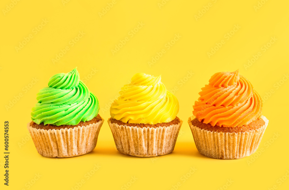 Tasty colorful cupcakes on yellow background