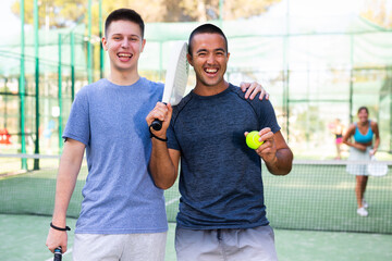 Wall Mural - Portrait of happy man and teenage boy padel tennis players standing on outdoor court.