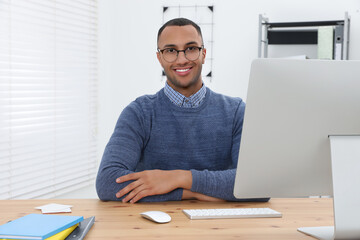 Canvas Print - Happy young intern working at table in modern office