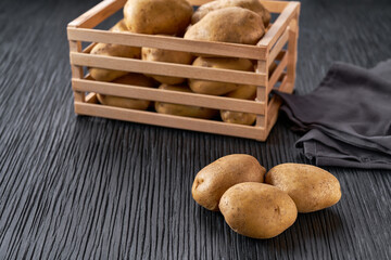 Wall Mural - fresh organic potato on dark wooden table with a potato box in the background.