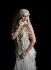 Wall Mural - Close up portrait of beautiful blonde female model wearing an extravagant pearl jewelled gown. Gestural arms reaching out,  isolated on a black studio background.