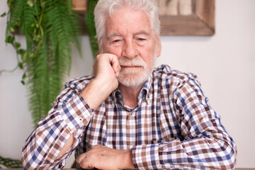 Wall Mural - Portrait of serious bearded senior man with hand on face looking down lost in thought while sitting at cafe table.