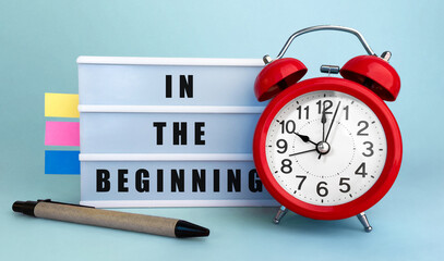 Fototapete - Text In the beginning written on the lightbox with alarm clock and colorfull stickers on blue background