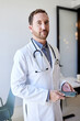 © Cavan Images - Portrait of male doctor holding smart phone while standing in clinic
