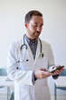 © Cavan Images - Male doctor surfing net through smart phone while standing in clinic