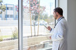 © Cavan Images - Side view of male doctor using smart phone while standing near window