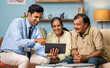 Indian banker showing investment or insurance plans on digital tablet to senior couple at home - concept of financial advisor, home banking service and professional occupation.