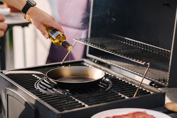 Wall Mural - Close-up of man add olive oil on frying carbon steel pan which is on the grill. 