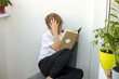 © Julia Jones - Tired boy sits on a chair with a book and holds his head with his hand