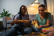 Two attractive girls, cheerful best friends having fun, drinking beer and cider and eating pizza at home. Pizza slice in hands