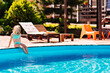 © andrey - Cute and funny blonde teenage girl in a swimsuit sits on the side of the pool.
