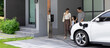 © InfiniteFlow - Progressive young parents and daughter with electric vehicle and home charging station. Green and clean energy from electric vehicles for healthy environment. Eco power from renewable source at home.
