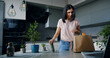 © serg - Beautiful satisfied young modern woman came back from food market with package with products and unpacking it near the kitchen table