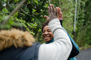 Wall Mural - Mother and daughter giving high-five during walk in park