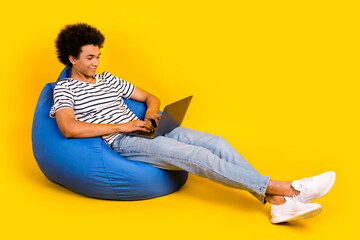 Poster - Full body size photo of young satisfied guy lying beanbag with netbook writing his graduation last exam isolated on yellow color background