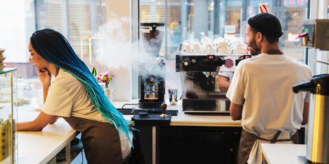 Smiling male barista making coffee, waitress standing next to him