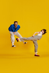 Wall Mural - Portrait with funny couple, actors woman and man playing out a fight on a stage over yellow studio background. Family quarrel, conflict