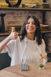 © Tatyana - Happy young dark-haired woman sitting in a cafe,showing a thumbs up.