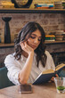 © Tatyana - A young attractive dark-haired woman is reading a book in a cafe.