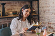 © Tatyana - A young attractive dark-haired woman is reading a book in a cafe.