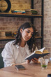 © Tatyana - A young attractive dark-haired woman is reading a book in a cafe.