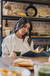 © Tatyana - A young attractive dark-haired woman is reading a book in a cafe and drinking green matcha tea.