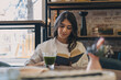 © Tatyana - A young attractive dark-haired woman is reading a book in a cafe and drinking green matcha tea.