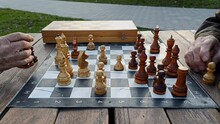 Two Elderly Men Play Chess In An Outdoor City Park. Chess Board And Wooden Chess Pieces.