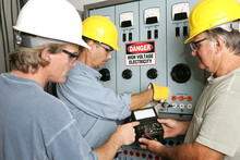 Group Of Electricians Using An OHM Meter To Test Voltage In An Industrial Power Center.  All Work Being Performed According To Industry Code And Safety Standards.  (note To Inspector: OHMS On The Mete
