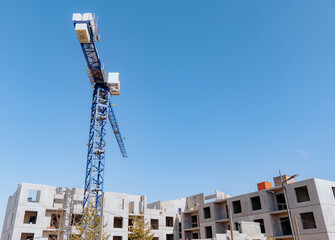 Wall Mural - High-rise building crane with a long arrow of blue color on blue clear sky above a concrete building under construction with solid walls