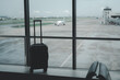 © waragron - Traveling by airplane. one suitcases in the airport departure lounge, vacation concept or business travel, airplane taking off on the background, luggage in waiting area airport terminal