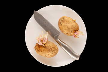 Two potatoes with sprouts with a metal knife on a white ceramic plate on a black background, macro, top view.