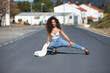 Young, beautiful, brunette woman with curly hair, white top, jeans and heels, crouched down posing in the middle of a lonely road. Concept beauty, fashion, posing, model.