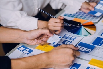 Close up ux developer and ui designer brainstorming about mobile app interface wireframe design on table with customer breif and color code at modern office.Creative digital development agency
