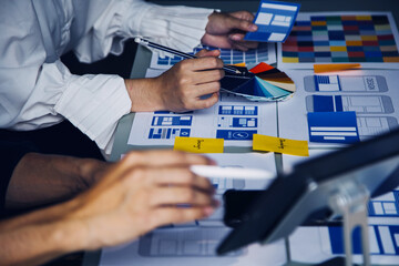 Close up ux developer and ui designer brainstorming about mobile app interface wireframe design on table with customer breif and color code at modern office.Creative digital development agency