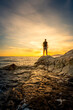 © Aytug Bayer - Young man standing on rocky beach at sunset time