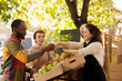© DC Studio - Vendor offering samples to customers while selling home-grown fruits and vegetables at local farmers market. Young multiracial family couple tasting natural organic produce while visiting food fair