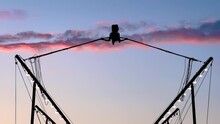Slow Motion: Silhouette Of Little Girl Is Jumping On Bungee Trampoline Against Twilight Sky After Sunset At Amusement Park. Childhood, Summer, Outdoor Activity And Holiday Concept