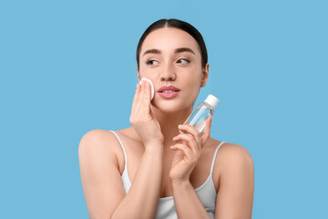 Wall Mural - Beautiful woman removing makeup with cotton pad on light blue background