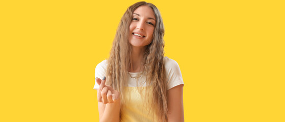 Wall Mural - Happy young woman making heart shape with her fingers on yellow background