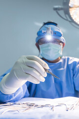 Wall Mural - Close up of surgeon's hand holding surgical knife or scalpel inside operating theatre with a blue uniform.The doctor with glove did surgery with light.People working in a hospital.