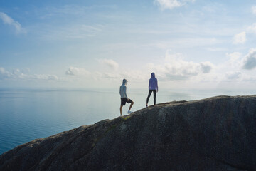 Two people standing on top of the mountain, looking at the ocean and the sky beneath, admire the wild beauty of seascape, natural beauty concept, copy space