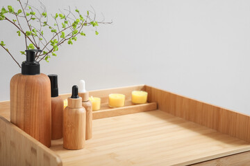 Bath accessories with candles and tree branches on table near light wall, closeup