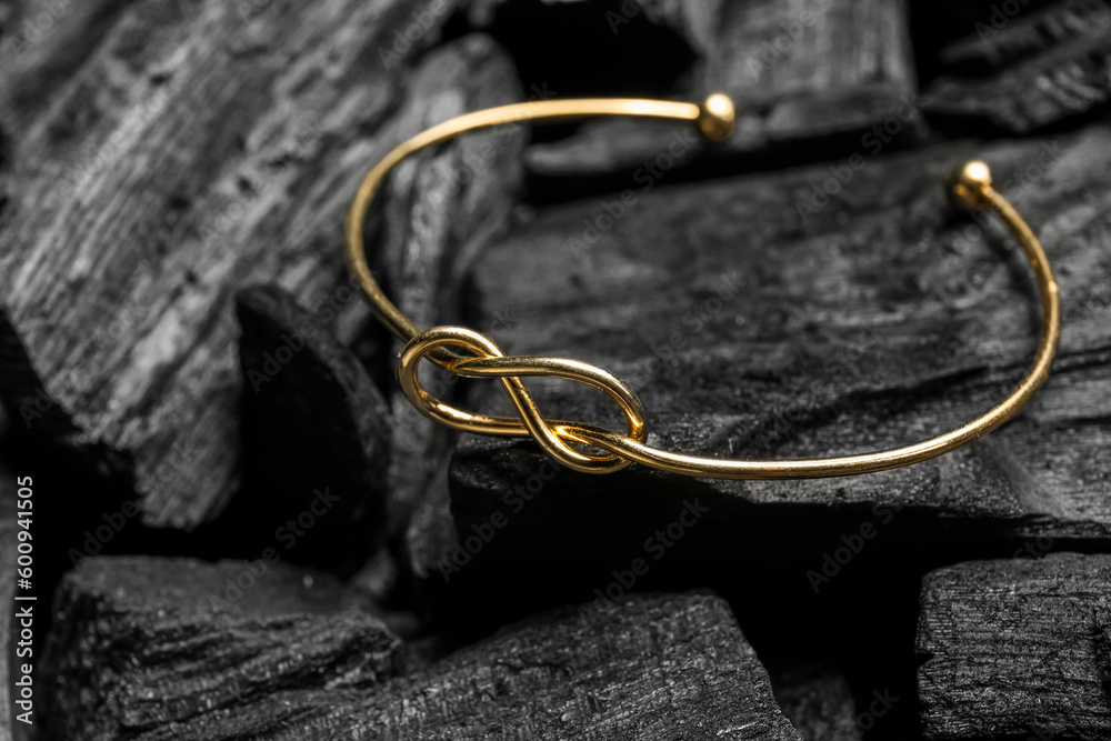 Golden bracelet on black charcoal, closeup