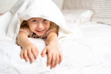 happy little girl in a white bed on a pillow, good morning, healthy baby sleep concept